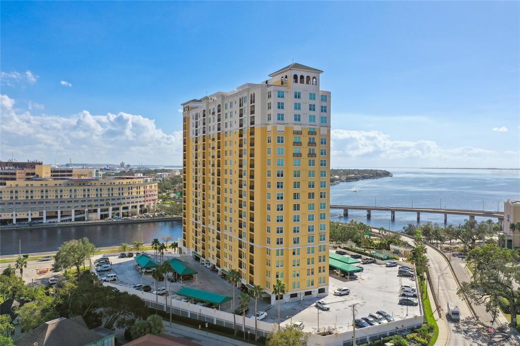 An aerial view shows a tall yellow residential tower with a parking lot and waterfront — 345 BAYSHORE BOULEVARD UNIT P9, TAMPA, FL