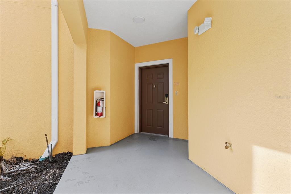 A covered entryway features a brown door, a wall-mounted fire extinguisher, and yellow stucco walls — 8801 WORLDQUEST BOULEVARD UNIT 4108, ORLANDO, FL