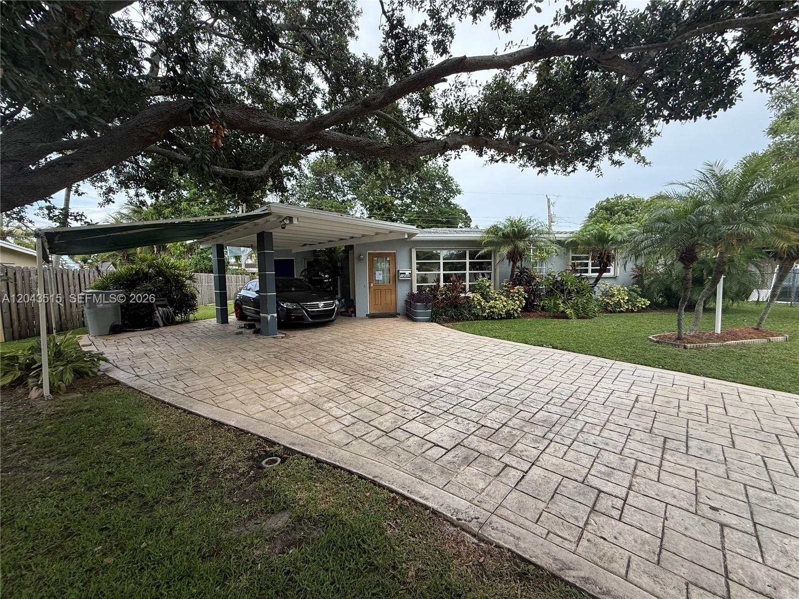 A single-story house features a large paved driveway, a carport, and mature landscaping — 1232 SW 1st Ave, Pompano Beach FL 33060, POMPANO BEACH, FL