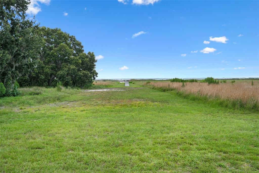 A grassy field leads to a wooden dock extending into a distant body of water — LAKE TOHOPEKALIGA BOULEVARD, KISSIMMEE, FL