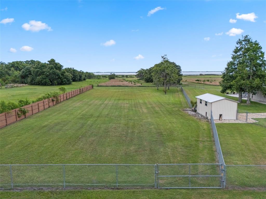 A large, fenced grassy backyard features a small shed and a distant view of water — LAKE TOHOPEKALIGA BOULEVARD, KISSIMMEE, FL