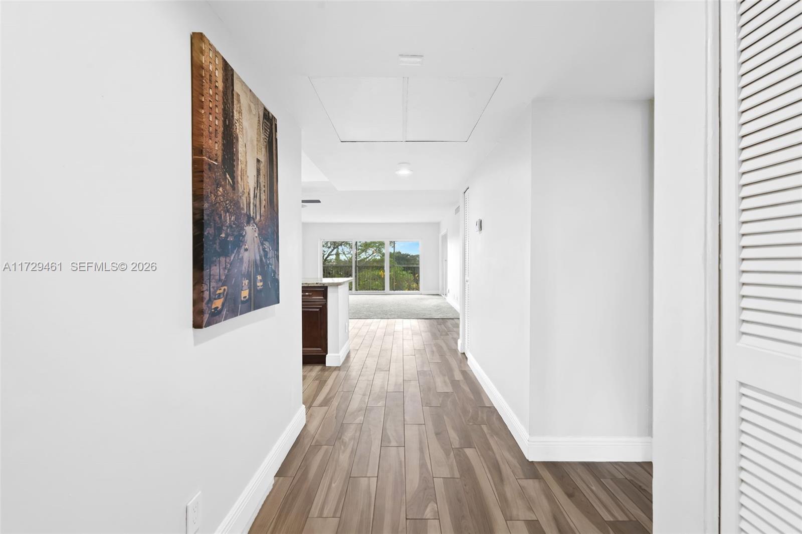 A hallway with wood-look tile flooring leads toward an open living area with large windows — 3050 N Palm Aire Dr # 501, Pompano Beach FL 33069, POMPANO BEACH, FL