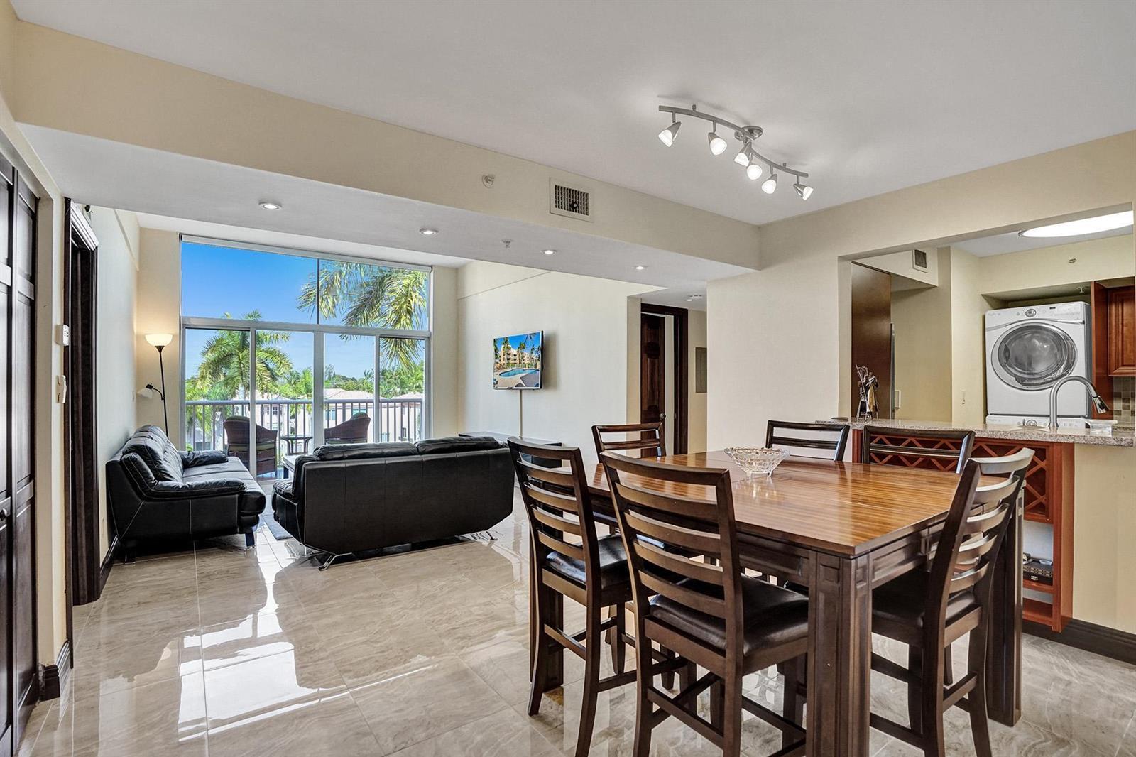 A living and dining area with tile floors, a wooden table, and a balcony view — 1350 SE 3rd Avenue # 406, Dania Beach FL 33004, DANIA BEACH, FL