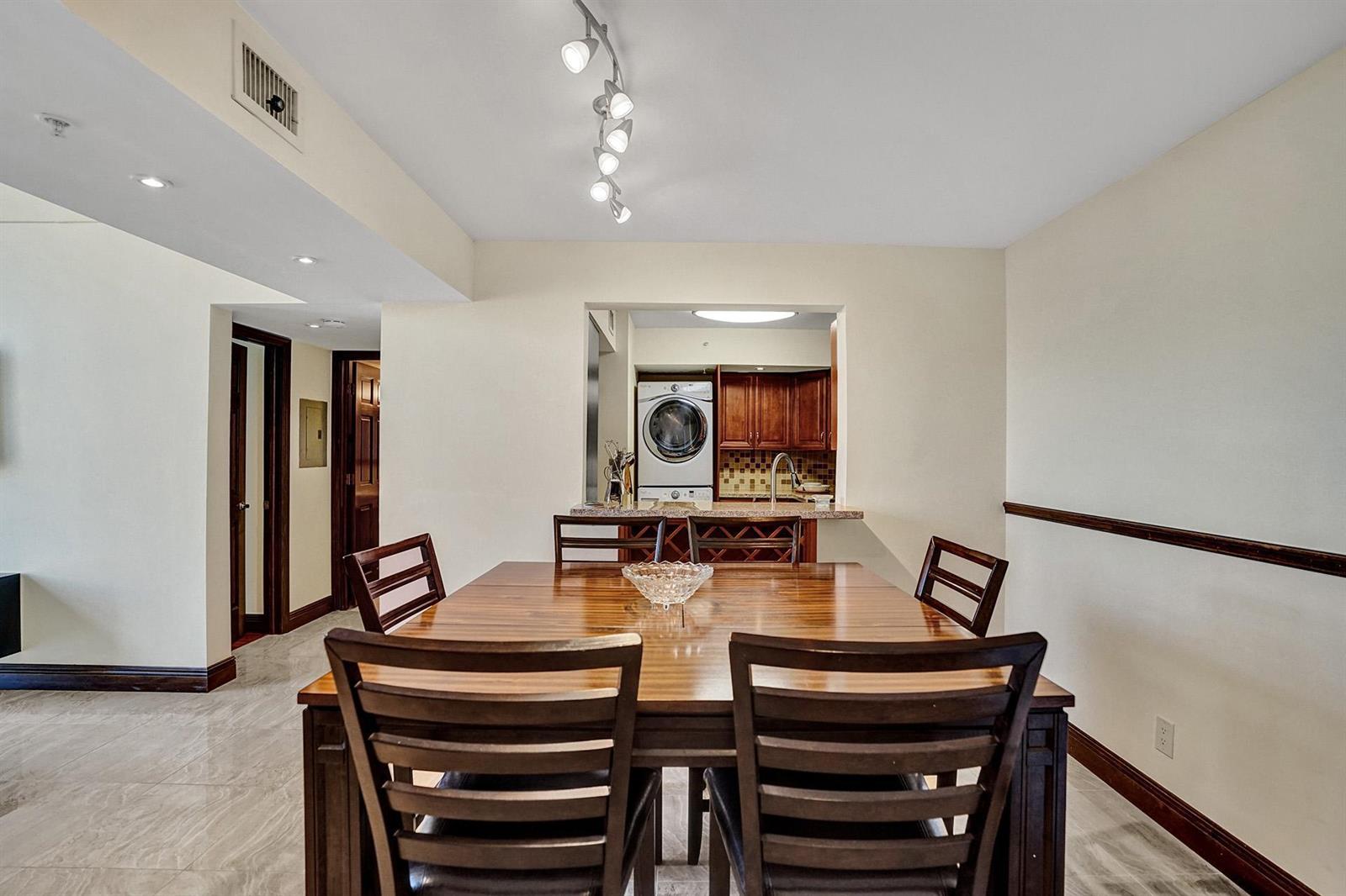 A dining room with a wooden table and chairs overlooks a kitchen with laundry appliances — 1350 SE 3rd Avenue # 406, Dania Beach FL 33004, DANIA BEACH, FL