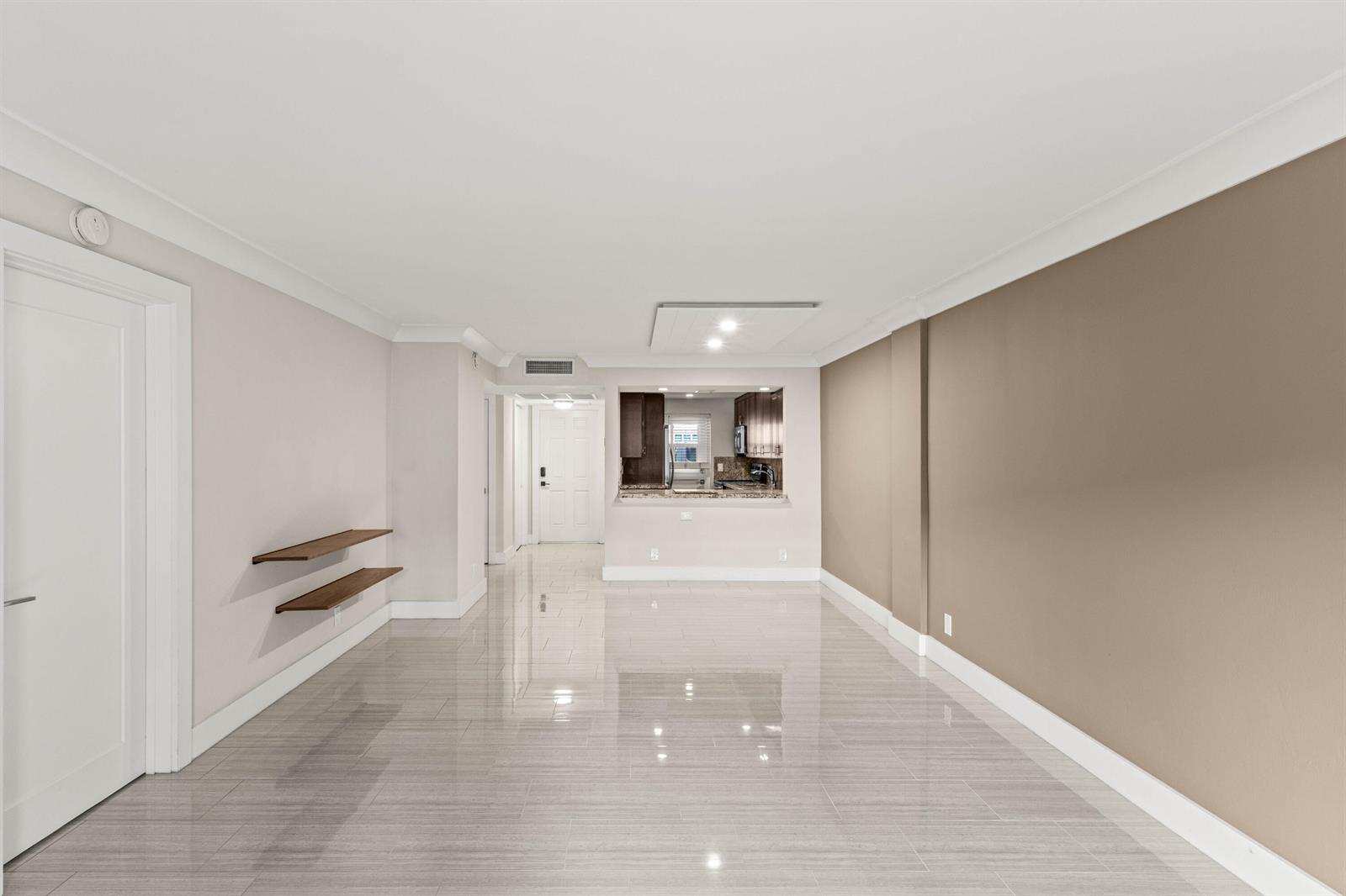 A living area with light-colored tile floors, two wall-mounted shelves, and a kitchen pass-through window — 4502 N Federal Highway # 144e, Lighthouse Point FL 33064, LIGHTHOUSE POINT, FL
