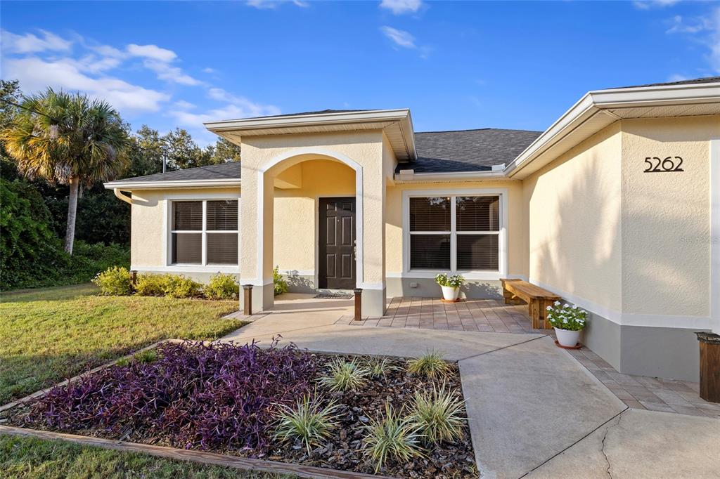 The exterior of a single-story house features a covered entryway, beige stucco, and landscaping — 5262 RHAPSODY AVENUE, NORTH PORT, FL