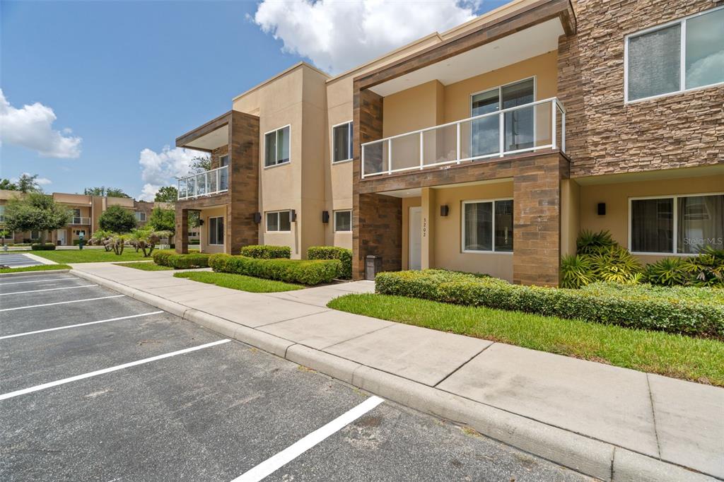 A two-story apartment building exterior features tan stucco, stone accents, balconies, and a parking lot — 3202 BRASILIA AVENUE, KISSIMMEE, FL