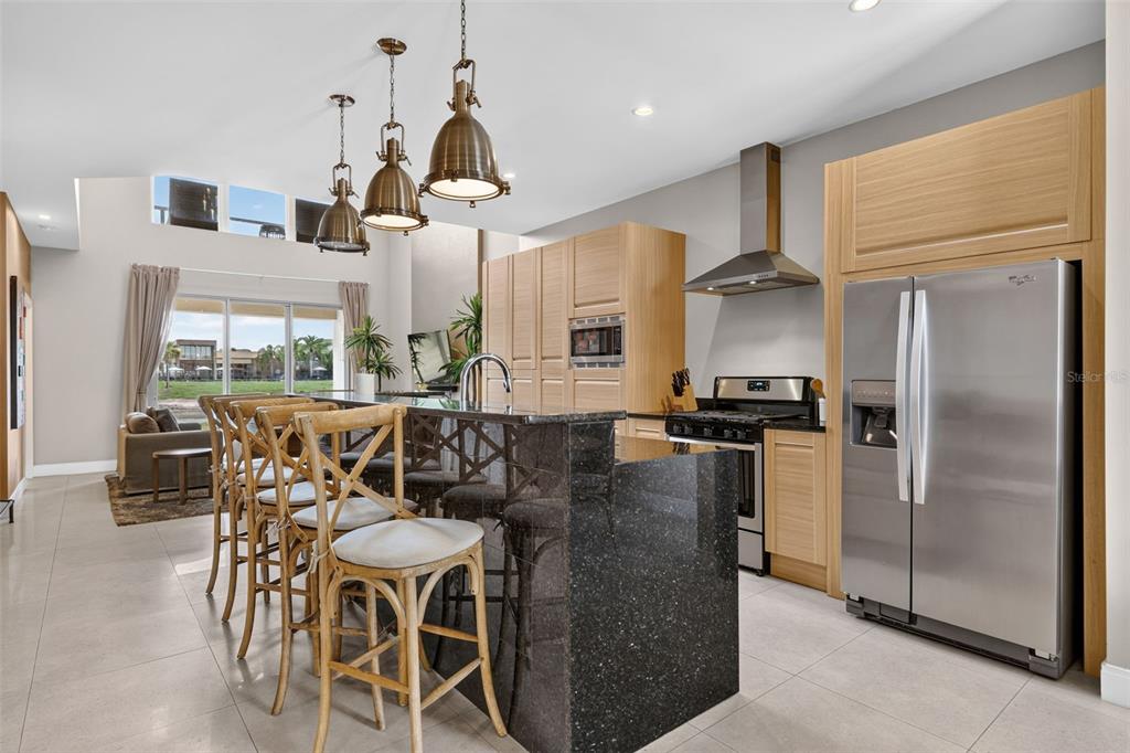 A modern kitchen features light wood cabinets, a dark granite island, and stainless steel appliances — 3202 BRASILIA AVENUE, KISSIMMEE, FL