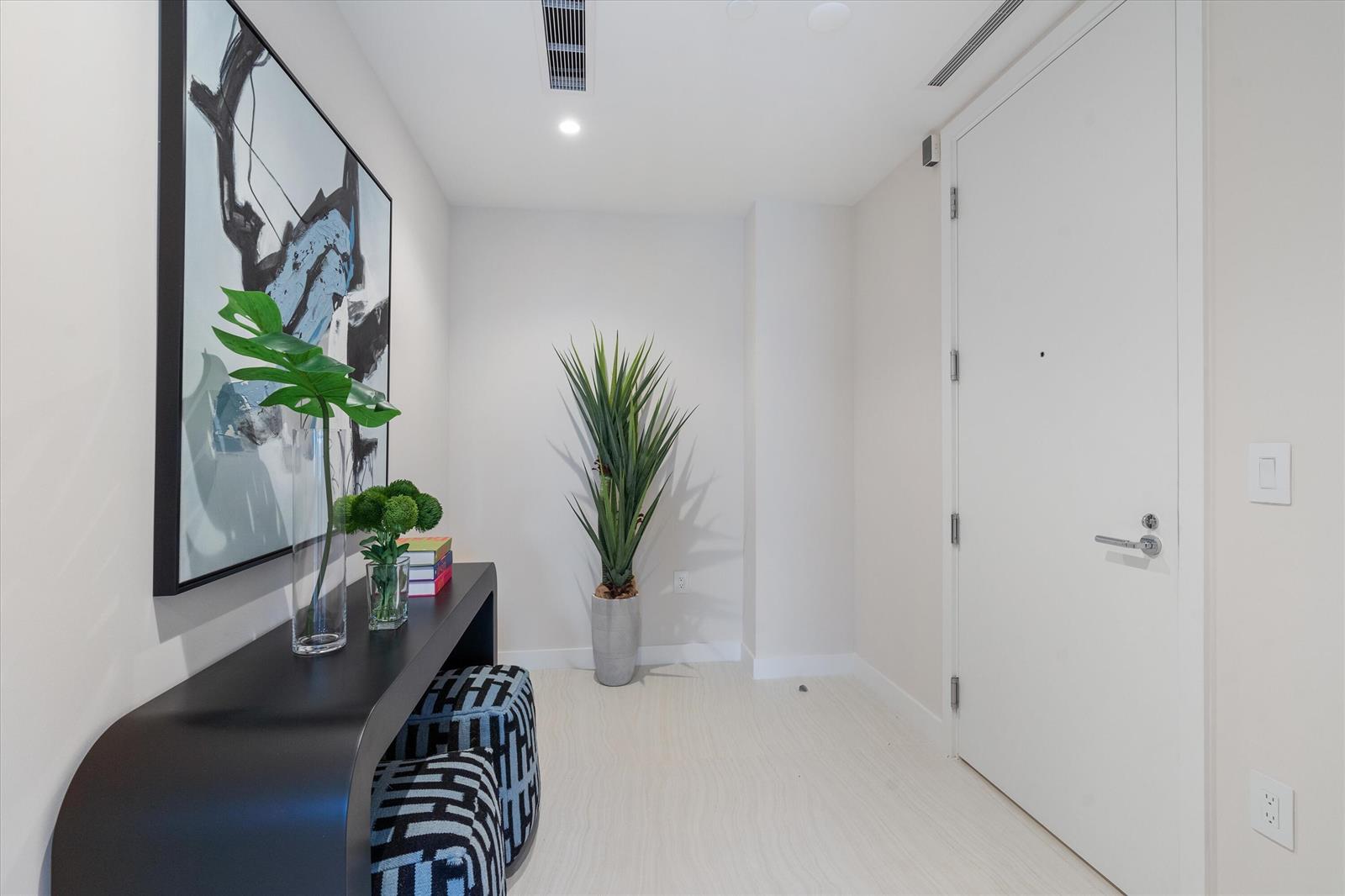 A modern entryway features a black console table, patterned ottomans, a tall plant, and artwork — 220 SE Mizner Boulevard # 604, Boca Raton FL 33432, BOCA RATON, FL