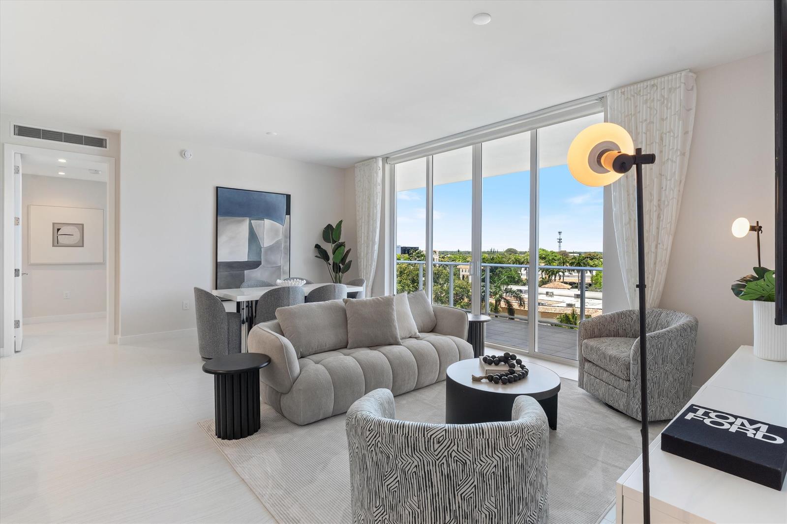 A modern living room features a textured sofa, patterned armchairs, and floor-to-ceiling windows with balcony access — 220 SE Mizner Boulevard # 604, Boca Raton FL 33432, BOCA RATON, FL