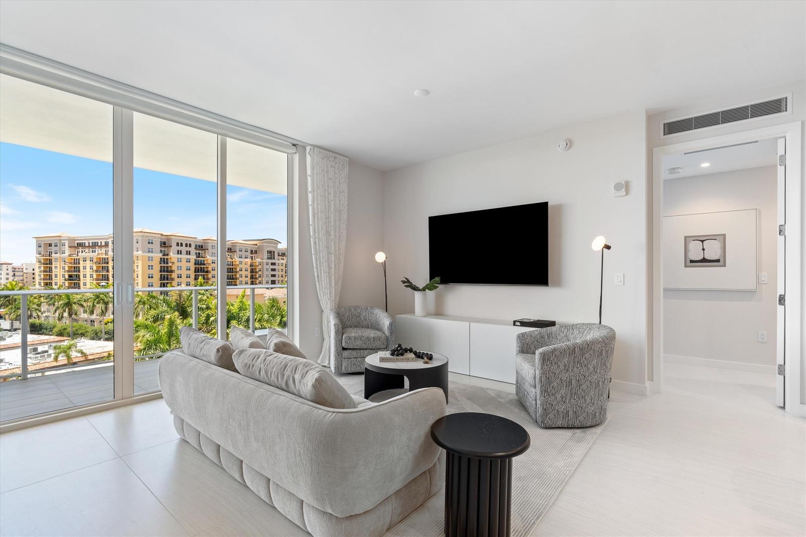 A modern living room features a sofa, two patterned armchairs, and a balcony with views — 220 SE Mizner Boulevard # 604, Boca Raton FL 33432, BOCA RATON, FL