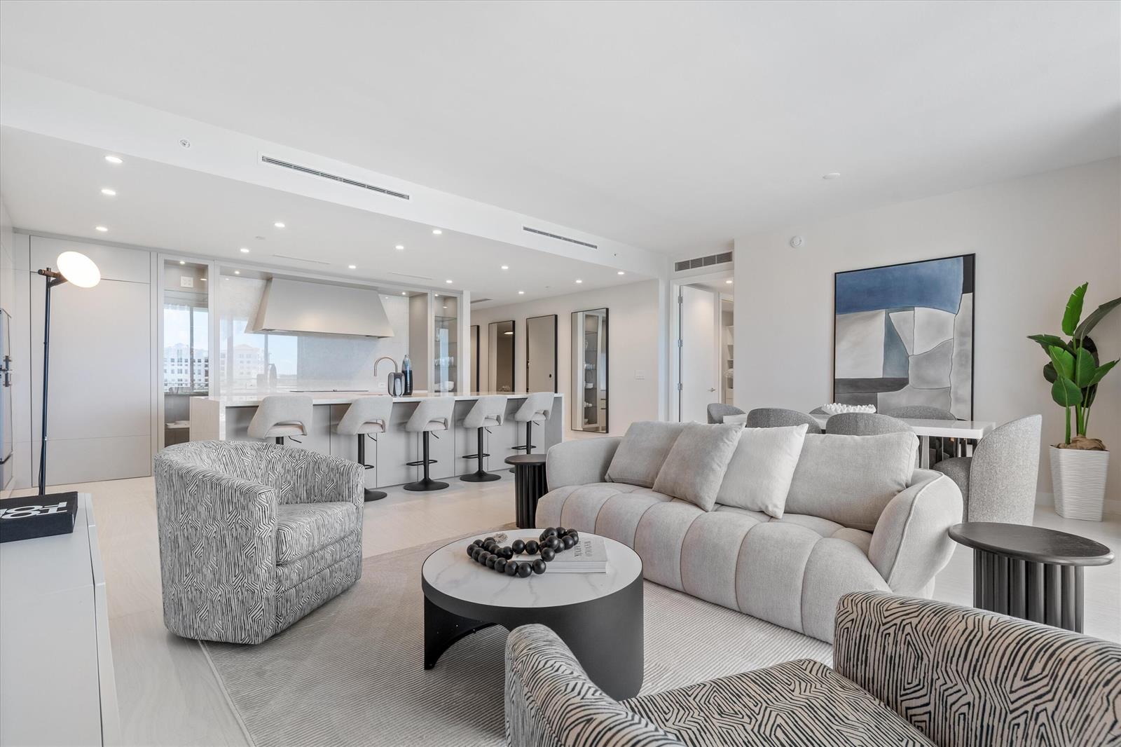 A modern open-concept living room features a kitchen island, neutral furniture, and light wood floors — 220 SE Mizner Boulevard # 604, Boca Raton FL 33432, BOCA RATON, FL