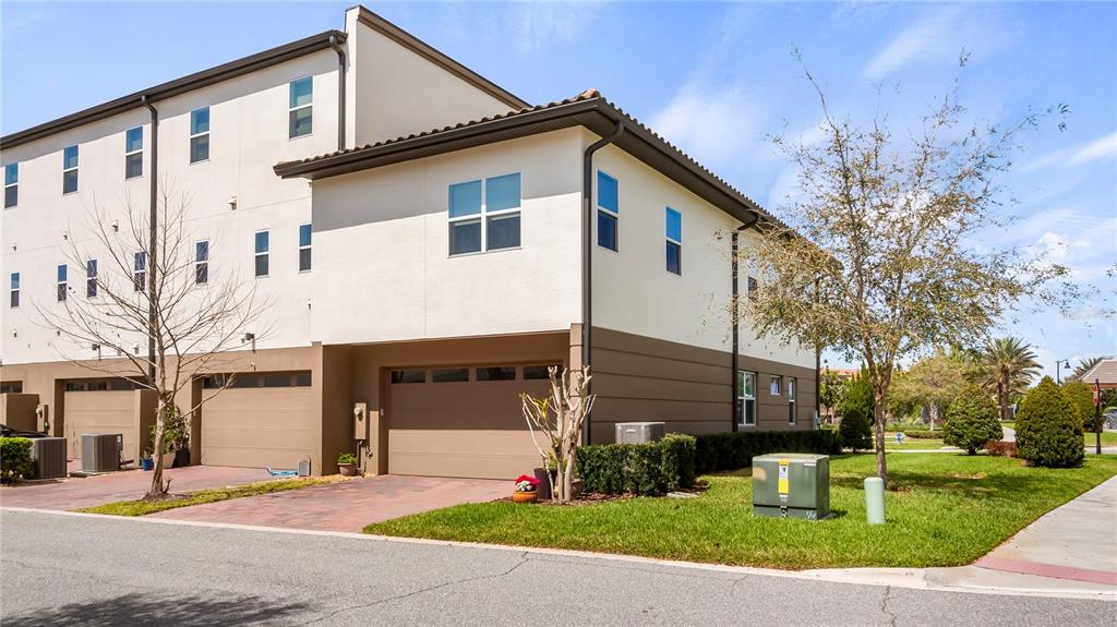 The exterior of a multi-story townhouse features tan stucco walls, brown garage doors, and landscaping — 9940 BUCKLOW HILL DRIVE, ORLANDO, FL