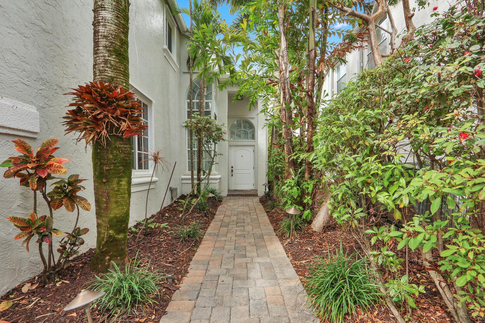 A stone walkway leads to a white front door framed by lush tropical landscaping — 2063 Cezanne Road, West Palm Beach FL 33409, WEST PALM BEACH, FL