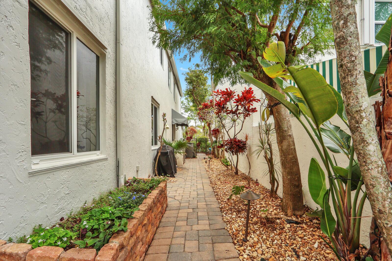 A paved walkway runs between a white building wall and a garden with stone landscaping — 2063 Cezanne Road, West Palm Beach FL 33409, WEST PALM BEACH, FL