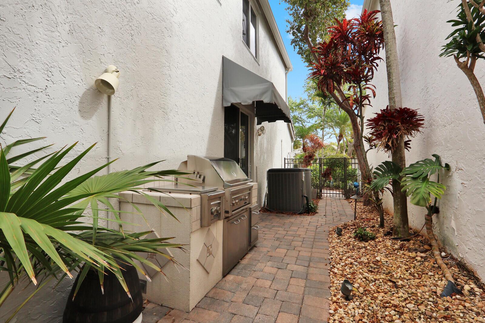 An outdoor patio features a built-in stainless steel grill, brick pavers, and tropical landscaping — 2063 Cezanne Road, West Palm Beach FL 33409, WEST PALM BEACH, FL
