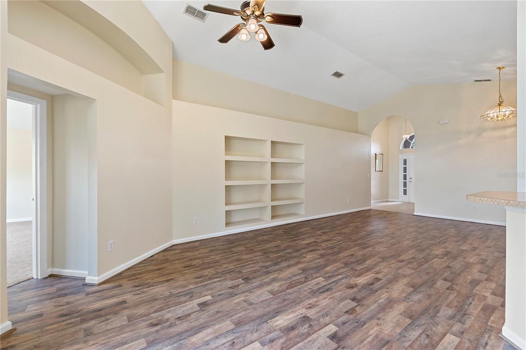 A living room with vaulted ceilings, wood-look flooring, and built-in wall shelving — 3103 MERLOT WAY, CLERMONT, FL