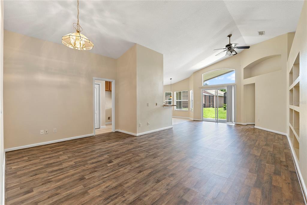 An empty living room features wood-look flooring, a vaulted ceiling, and a built-in wall shelf — 3103 MERLOT WAY, CLERMONT, FL