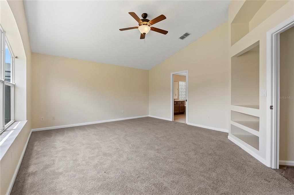 A carpeted bedroom features a vaulted ceiling, a ceiling fan, and built-in wall shelving — 3103 MERLOT WAY, CLERMONT, FL