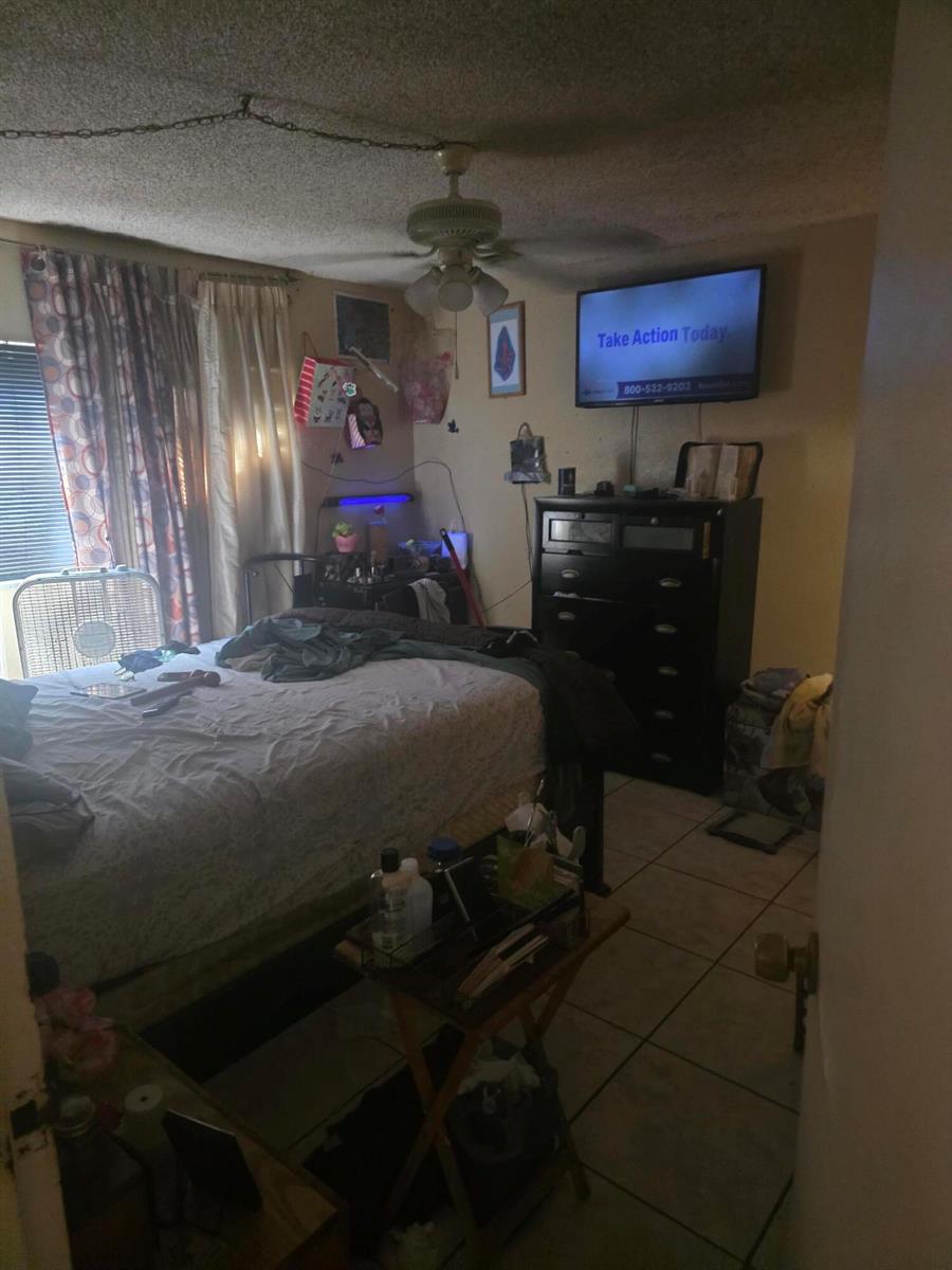 A bedroom features a bed, a dark dresser with a wall-mounted television, and tile flooring — 4101 NW 26th # 166, Lauderhill FL 33313, LAUDERHILL, FL