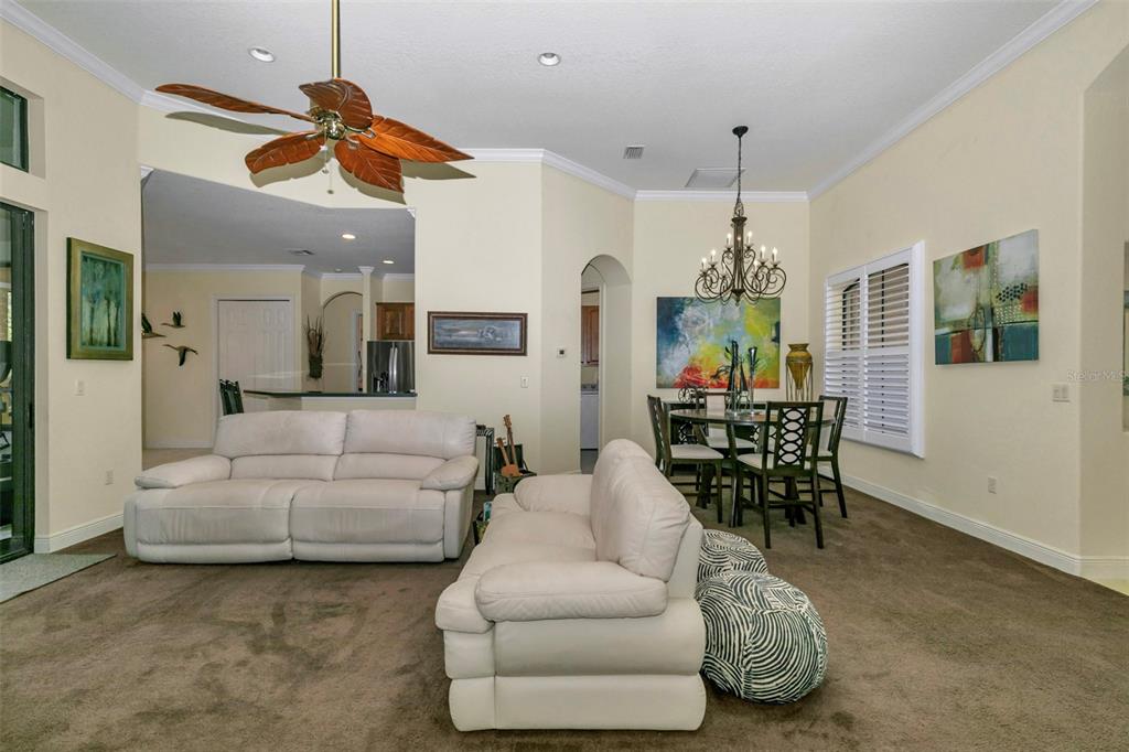 A living and dining area with beige walls, brown carpeting, and a palm-leaf ceiling fan — 5203 GROVE MANOR, LADY LAKE, FL