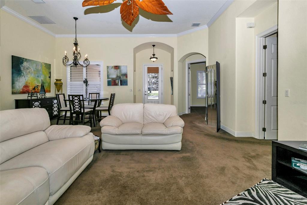 A living room with beige carpet, two white sofas, and an adjacent dining area — 5203 GROVE MANOR, LADY LAKE, FL
