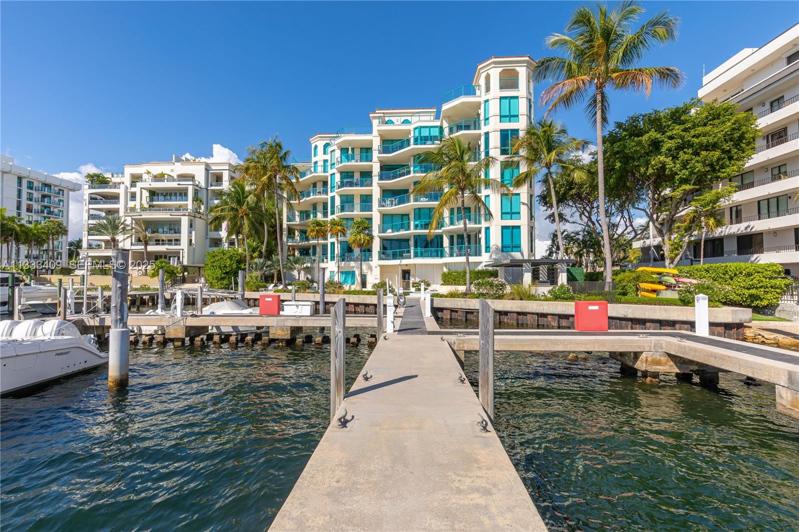 A concrete dock extends toward a multi-story waterfront apartment building surrounded by palm trees — 1660 W Glencoe St # 302, Coconut Grove FL 33133, COCONUT GROVE, FL
