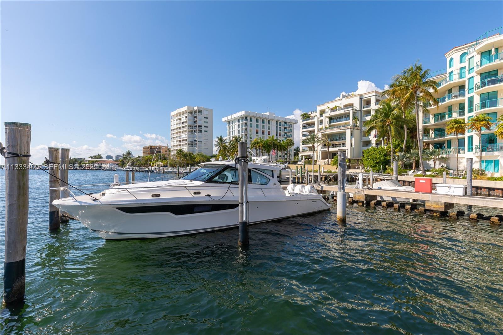 A white motorboat is docked at a pier in front of several waterfront apartment buildings — 1660 W Glencoe St # 302, Coconut Grove FL 33133, COCONUT GROVE, FL