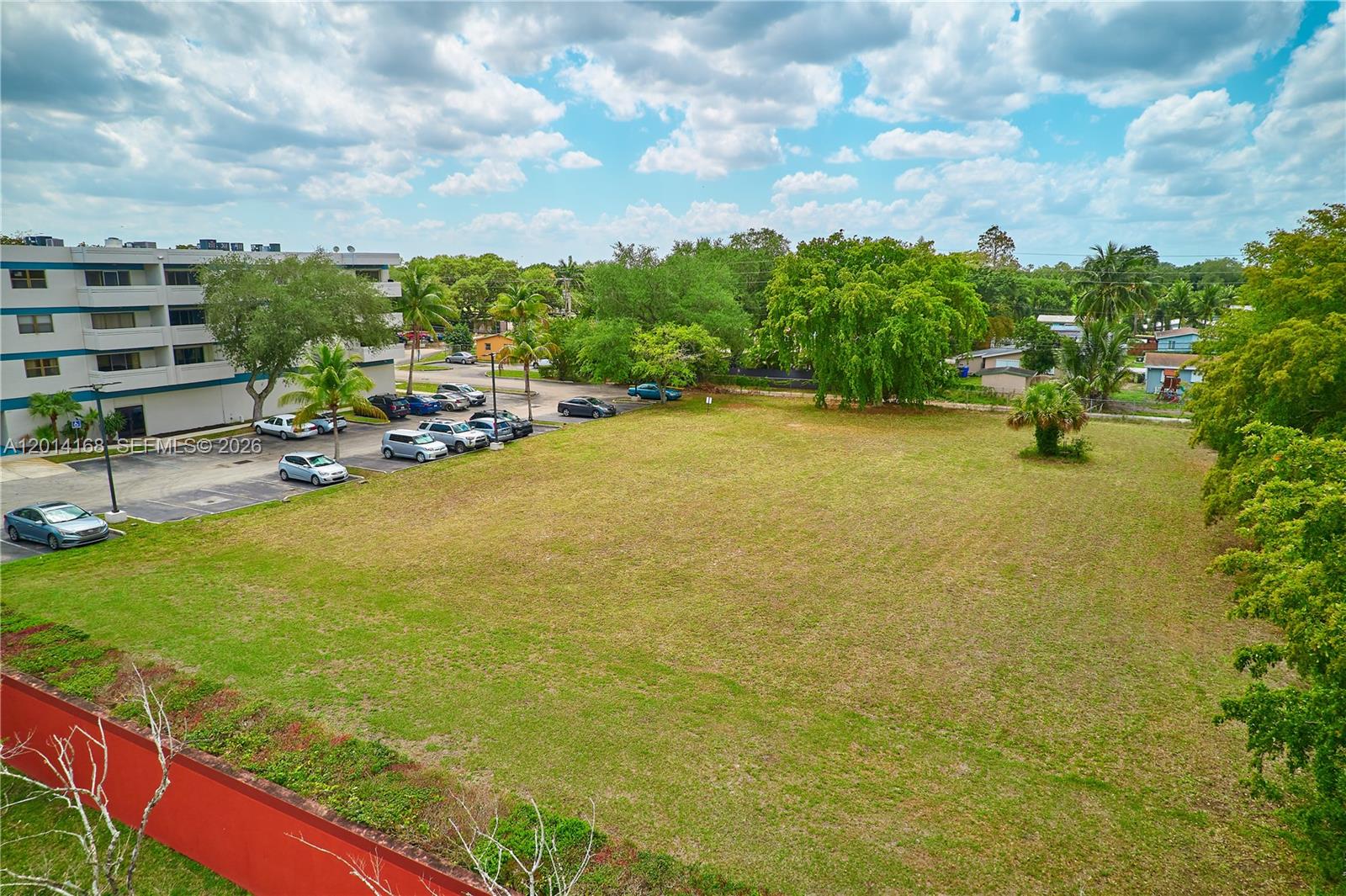 An aerial view shows a large, grassy vacant lot adjacent to a parking area and building — 0 N 61  Avenue, Hollywood FL 33024, HOLLYWOOD, FL