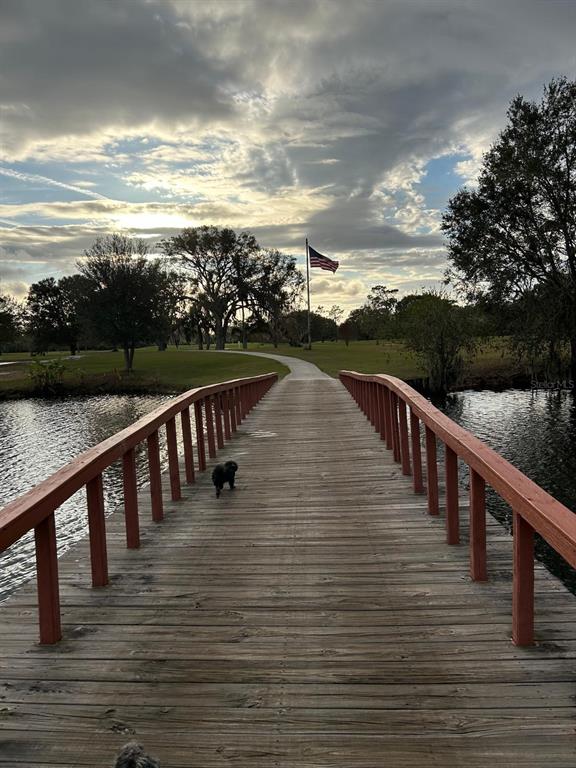 A wooden footbridge with red railings leads toward a grassy park with an American flag — 709 BELMONTE DRIVE, INDIAN LAKE ESTATES, FL