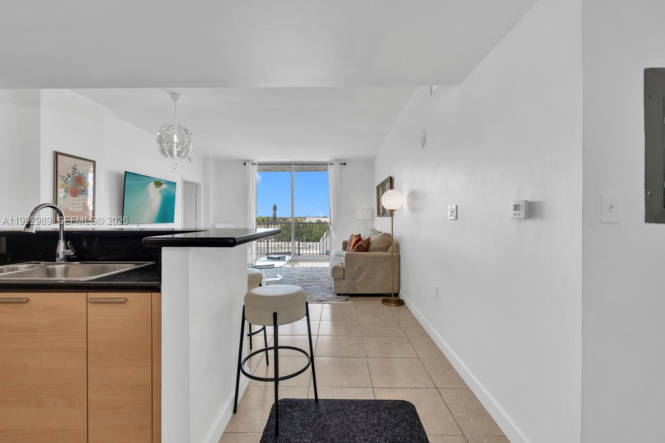 A kitchen with light wood cabinets and a black countertop overlooks a bright living area — 140 S Dixie Hwy # 403, Hollywood FL 33020, HOLLYWOOD, FL