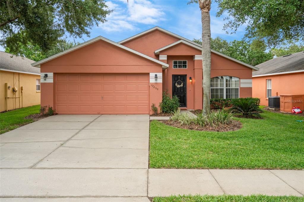 A single-story house with a terracotta-colored exterior, a two-car garage, and a front lawn — 17650 WOODCREST WAY, CLERMONT, FL