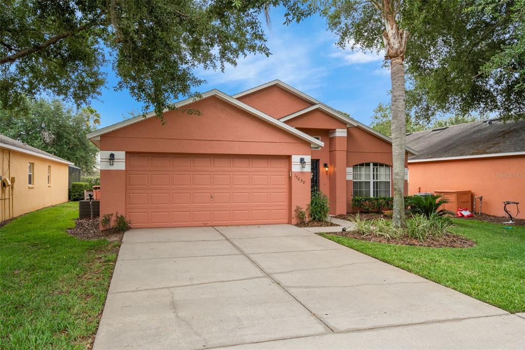 A single-story peach-colored house features a two-car garage and a concrete driveway — 17650 WOODCREST WAY, CLERMONT, FL