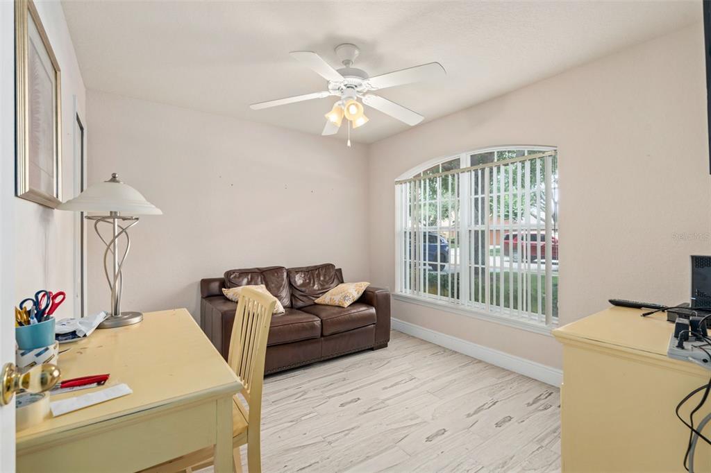 A home office features a brown leather loveseat, light wood-look flooring, and a ceiling fan — 17650 WOODCREST WAY, CLERMONT, FL