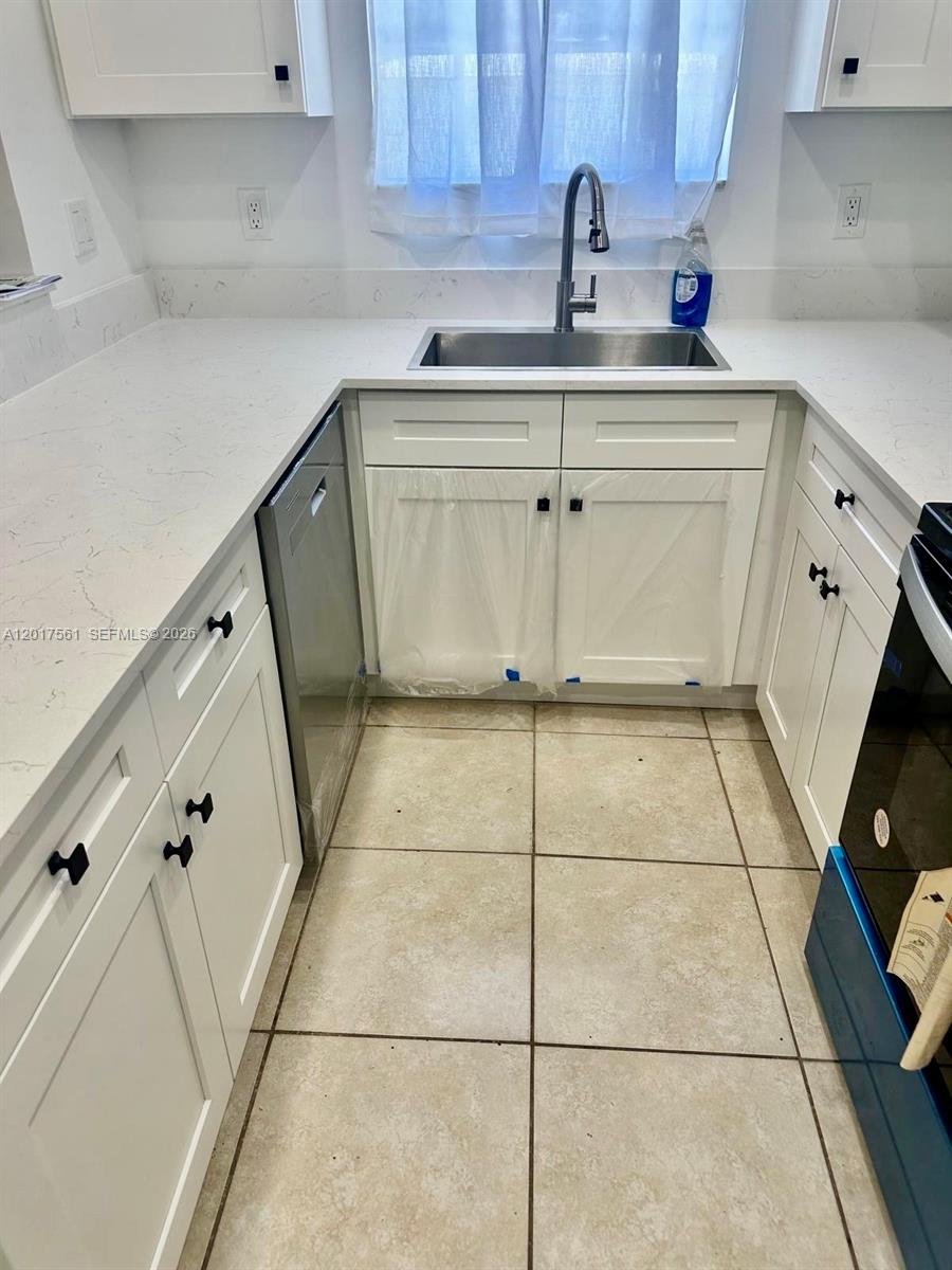 A white kitchen features quartz countertops, stainless steel appliances, and light-colored tile flooring — 2301 Wilson St # A, Hollywood FL 33020, HOLLYWOOD, FL