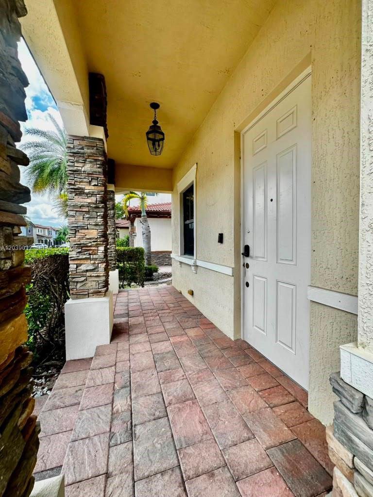 A covered front porch features stone-clad columns, a paved floor, and a white front door — 9825 NW 86th Ter, Doral FL 33178, DORAL, FL