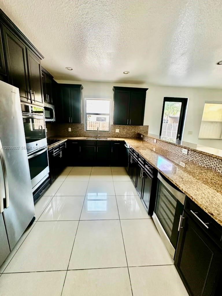 A kitchen features dark wood cabinets, granite countertops, stainless steel appliances, and light tile flooring — 9825 NW 86th Ter, Doral FL 33178, DORAL, FL