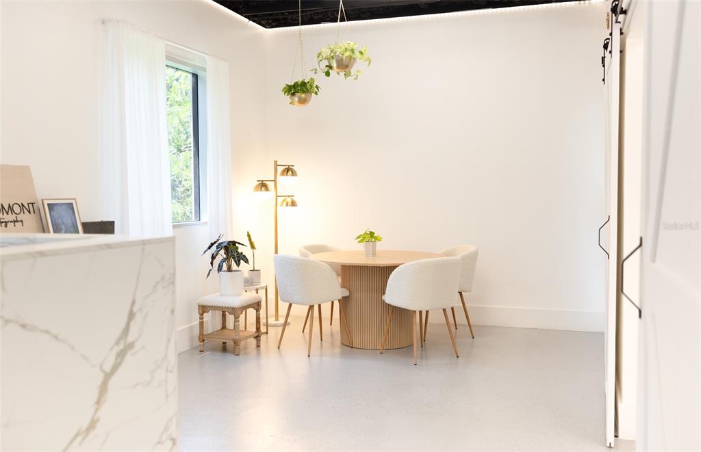 A dining area features a round fluted table, four white chairs, and hanging plants — 120 E MARKS STREET UNIT 200, ORLANDO, FL