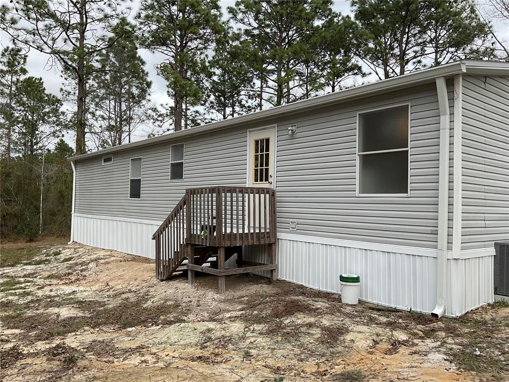 The exterior of a manufactured home features light gray siding, a wooden deck, and white skirting — 90 NE 132ND TERRACE, WILLISTON, FL