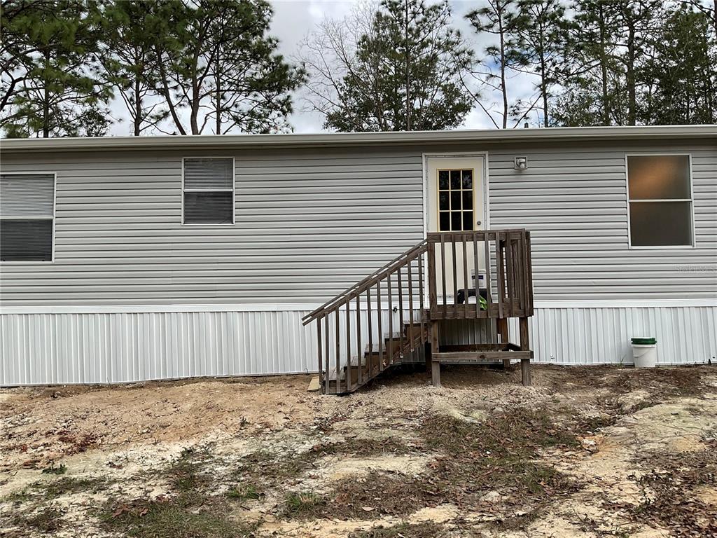 The exterior of a light gray mobile home features a wooden staircase leading to a door — 90 NE 132ND TERRACE, WILLISTON, FL