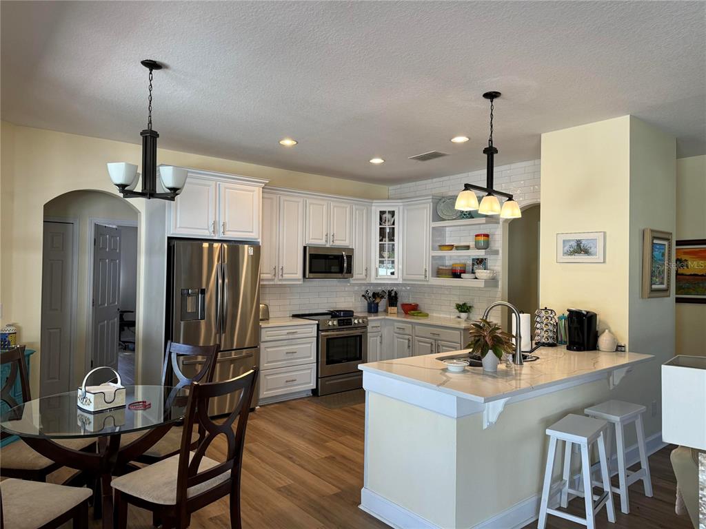 A kitchen features white cabinets, stainless steel appliances, a center island, and wood-look flooring — 2127 BRISTOL GRANDE WAY, ORLANDO, FL