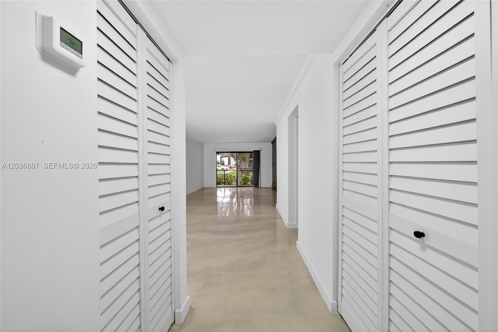 A hallway with white louvered closet doors leads to an open living area with glass doors — 265 SE 10th St # 1C, Deerfield Beach FL 33441, DEERFIELD BEACH, FL