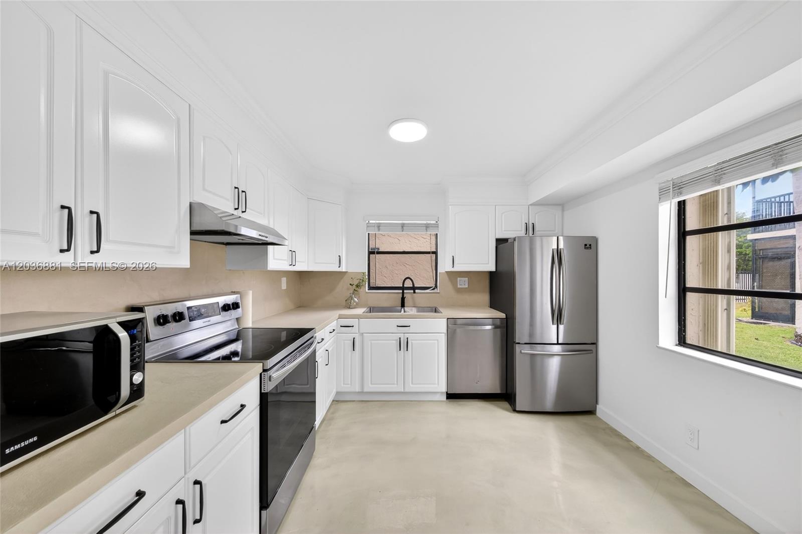 A kitchen features white cabinets, stainless steel appliances, beige countertops, and a window view — 265 SE 10th St # 1C, Deerfield Beach FL 33441, DEERFIELD BEACH, FL