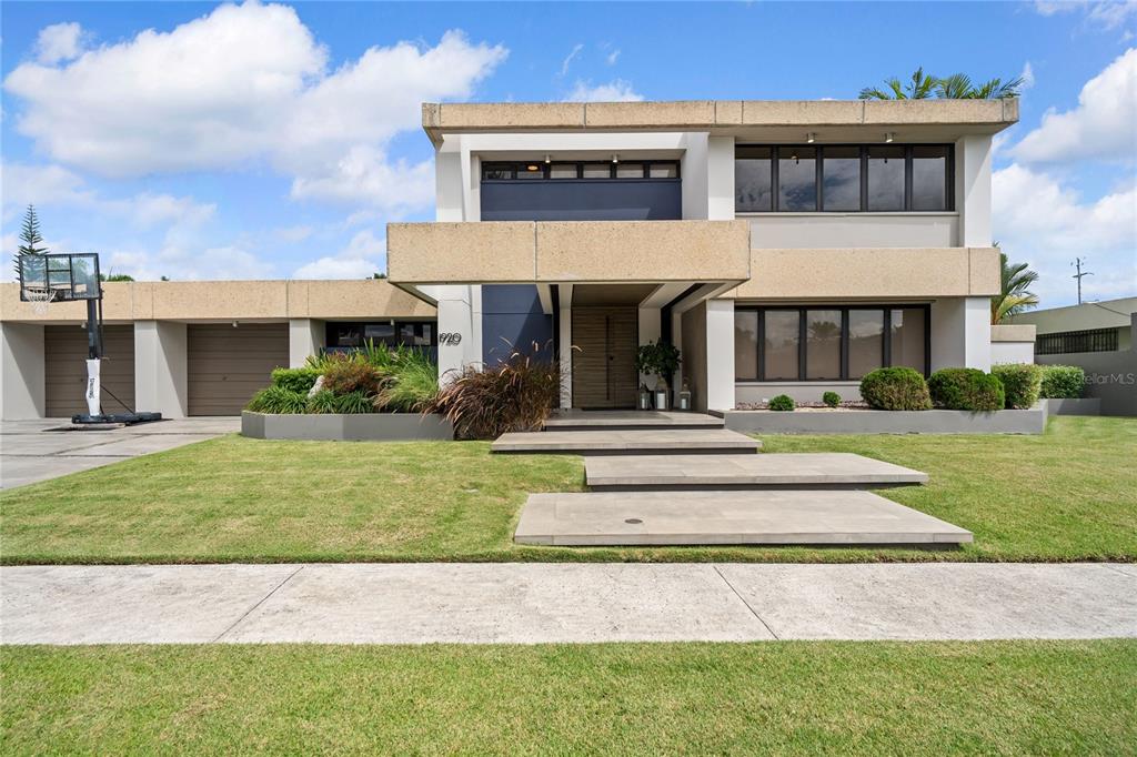 A modern two-story house features a flat roof, tan concrete accents, and a paved walkway — 1920 Petunia St URB. SANTA MARIA, SAN JUAN, PR