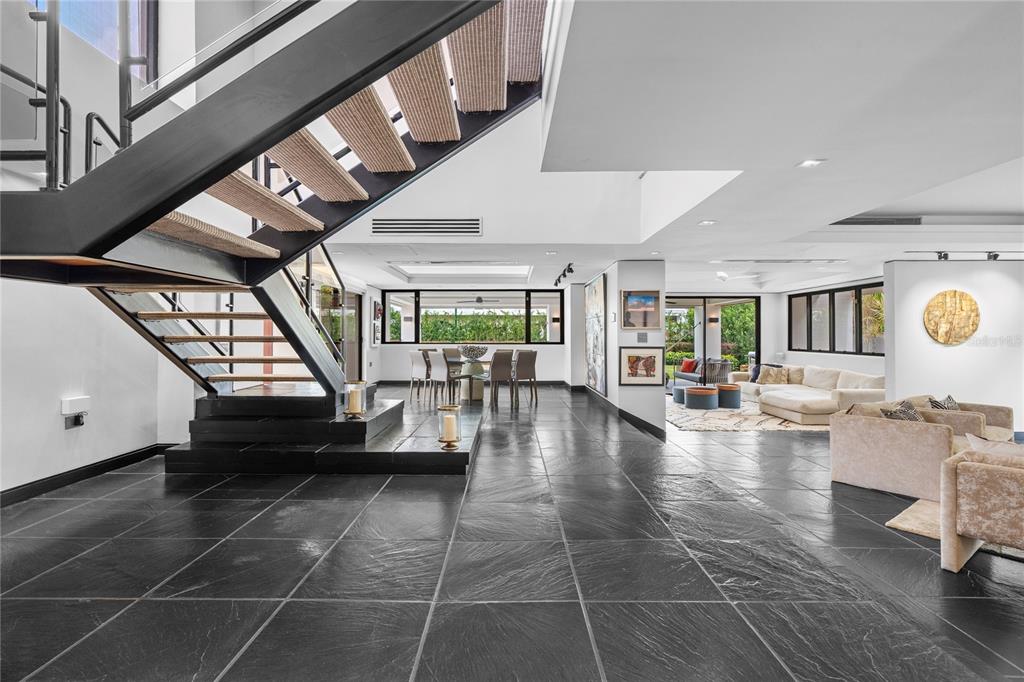 A modern living room features a floating staircase, dark stone flooring, and large glass doors — 1920 Petunia St URB. SANTA MARIA, SAN JUAN, PR