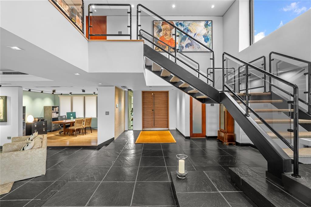 A modern foyer features dark stone flooring, a floating staircase, and an open office area — 1920 Petunia St URB. SANTA MARIA, SAN JUAN, PR