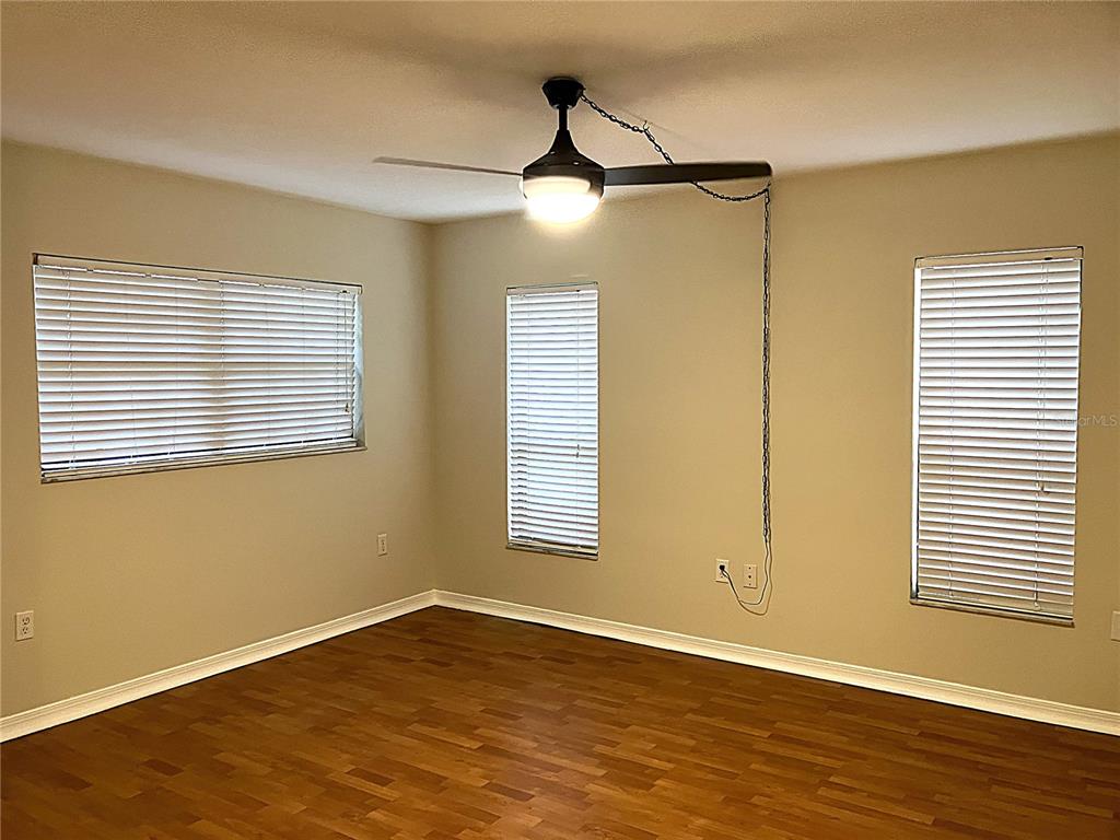 An empty room features wood-look flooring, beige walls, three windows with blinds, and a ceiling fan — 956 5TH STREET UNIT 9A, CLERMONT, FL