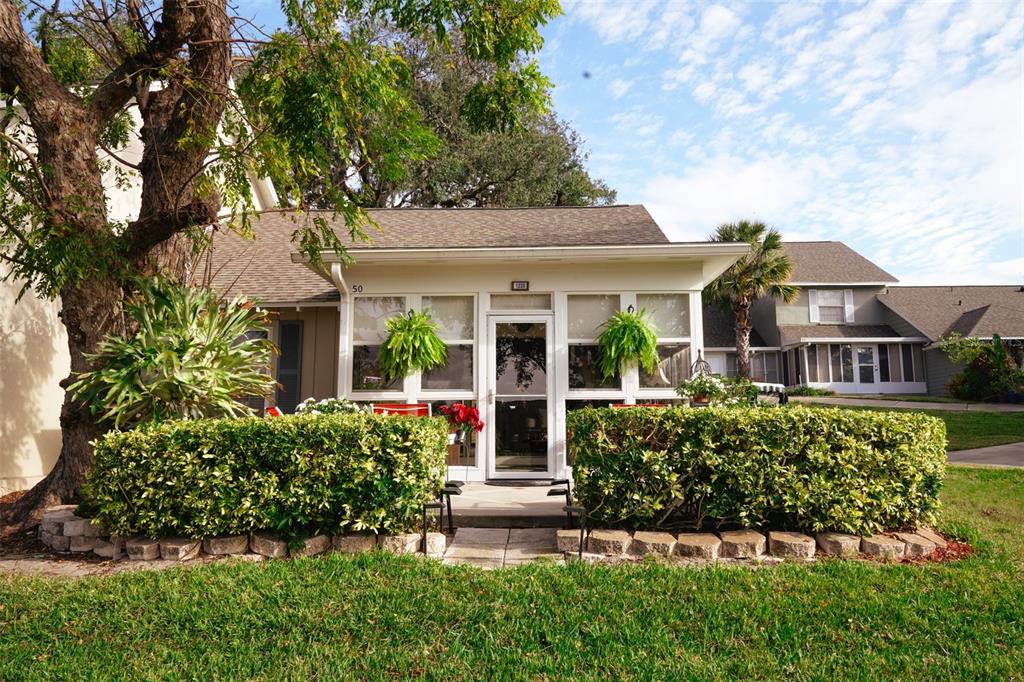 A single-story home with a screened-in front porch, manicured hedges, and a large tree — 1339 VILLA LANE UNIT 50, APOPKA, FL