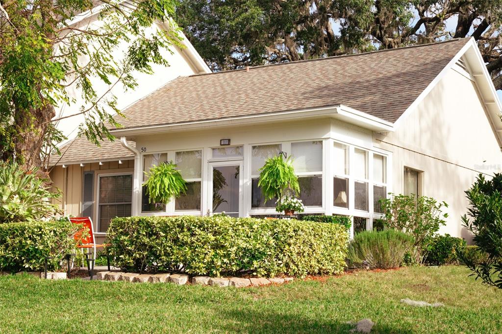 A beige house features a glass-enclosed sunroom, a manicured hedge, and a grassy front yard — 1339 VILLA LANE UNIT 50, APOPKA, FL