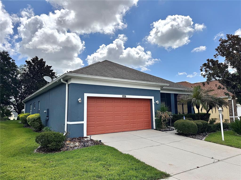 A blue house with a red garage door and a concrete driveway under a cloudy sky — 3447 MOUNT HOPE LOOP, LEESBURG, FL
